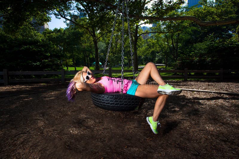 Young Blonde Athletic woman sitting and rocking on a tire swing in Central Park. Young Blonde Athletic woman sitting and rocking on a tire swing in Central Park
