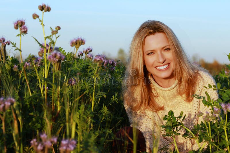 Mujer atractiva de la Edad Media que se sienta en un campo de flor de la lila imágenes de archivo libres de regalías Mujer atractiva de la Edad Media que se sienta en un campo de flor de la lila imágenes de archivo libres de regalías