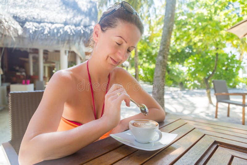 Mujer atractiva en bikini que goza del café en la barra del aire libre, fondo tropical imágenes de archivo libres de regalías Mujer atractiva en bikini que goza del café en la barra del aire libre, fondo tropical imágenes de archivo libres de regalías