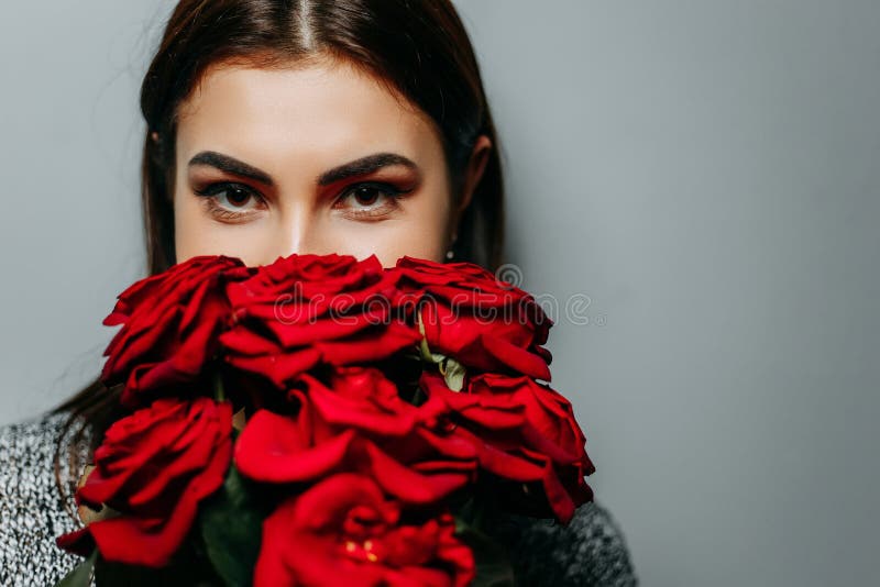Mujer atractiva hermosa joven que oculta detrás de rosas rojas Muchacha w imagen de archivo libre de regalías Mujer atractiva hermosa joven que oculta detrás de rosas rojas Muchacha w imagen de archivo libre de regalías