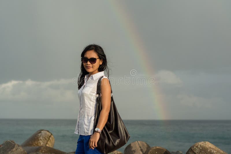 Mujer bastante asiática que coloca el arco iris cercano después de lluvia imágenes de archivo libres de regalías Mujer bastante asiática que coloca el arco iris cercano después de lluvia imágenes de archivo libres de regalías