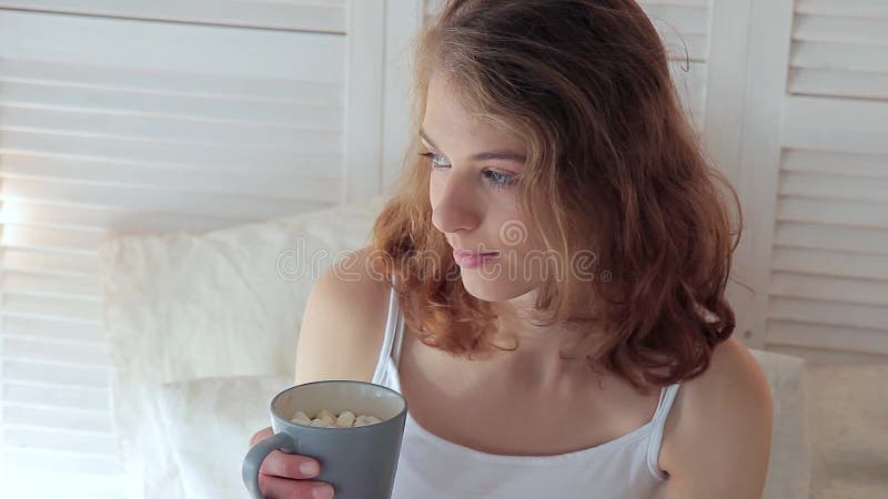 Mujer bastante joven que sostiene una taza de café caliente con la melcocha