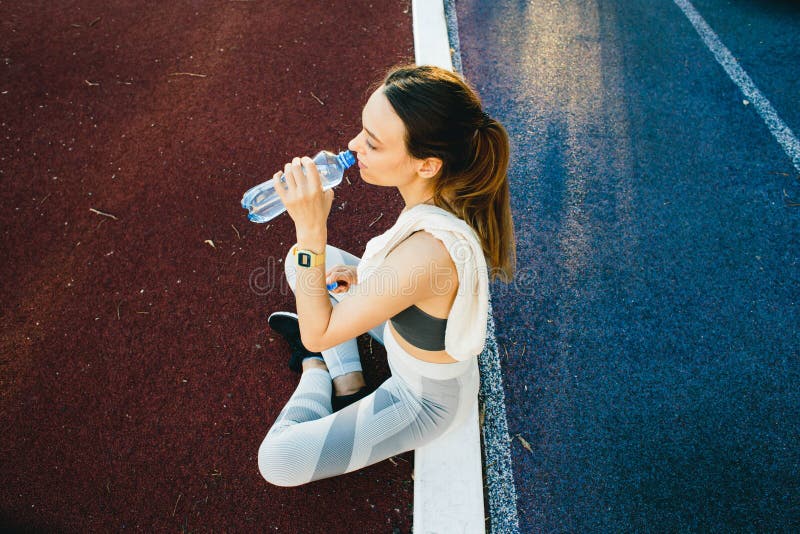 Mujer bonita que se sienta en la tierra con una botella de agua después de aire libre que activa imagenes de archivo Mujer bonita que se sienta en la tierra con una botella de agua después de aire libre que activa imagenes de archivo