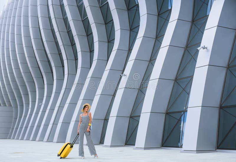 Mujer caucásica elegante joven en el aeropuerto con una maleta y un sombrero de paja imagenes de archivo Mujer caucásica elegante joven en el aeropuerto con una maleta y un sombrero de paja imagenes de archivo