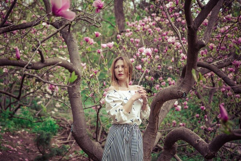 Mujer caucásica hermosa joven en el jardín floreciente de la primavera de magnolias La muchacha en el jardín en un día nublado imágenes de archivo libres de regalías Mujer caucásica hermosa joven en el jardín floreciente de la primavera de magnolias La muchacha en el jardín en un día nublado imágenes de archivo libres de regalías