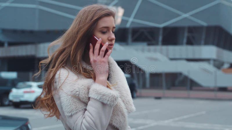 Mujer caucásica joven atractiva que sale del coche lujoso, hablando por el teléfono Mirada de moda, pelo rizado