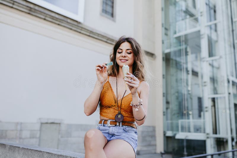 Mujer caucásica joven hermosa que come el helado de la menta en la calle de la ciudad en un día soleado Sonrisa feliz de la cara imagenes de archivo Mujer caucásica joven hermosa que come el helado de la menta en la calle de la ciudad en un día soleado Sonrisa feliz de la cara imagenes de archivo