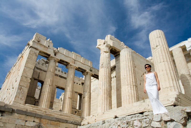 Young woman dressed white near the columns of entrance propylaea to ancient temple Parthenon in Acropolis Athens Greece on blue sky background. Young woman dressed white near the columns of entrance propylaea to ancient temple Parthenon in Acropolis Athens Greece on blue sky background