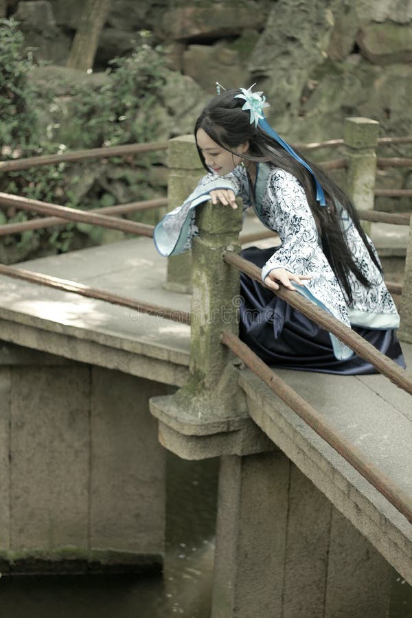 Mujer china asiática en el vestido azul y blanco tradicional de Hanfu, juego en una subida famosa del jardín en el puente doblado fotografía de archivo libre de regalías Mujer china asiática en el vestido azul y blanco tradicional de Hanfu, juego en una subida famosa del jardín en el puente doblado fotografía de archivo libre de regalías