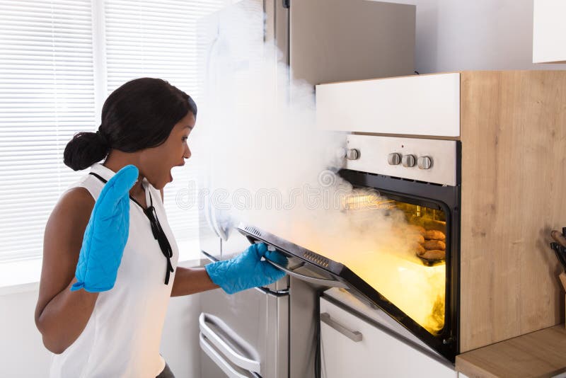 Mujer chocada que mira las galletas quemadas en horno