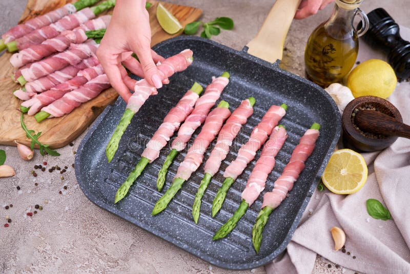 Mujer cocinando espárragos cubiertos de tocino en una sartén frita a la parrilla foto de archivo