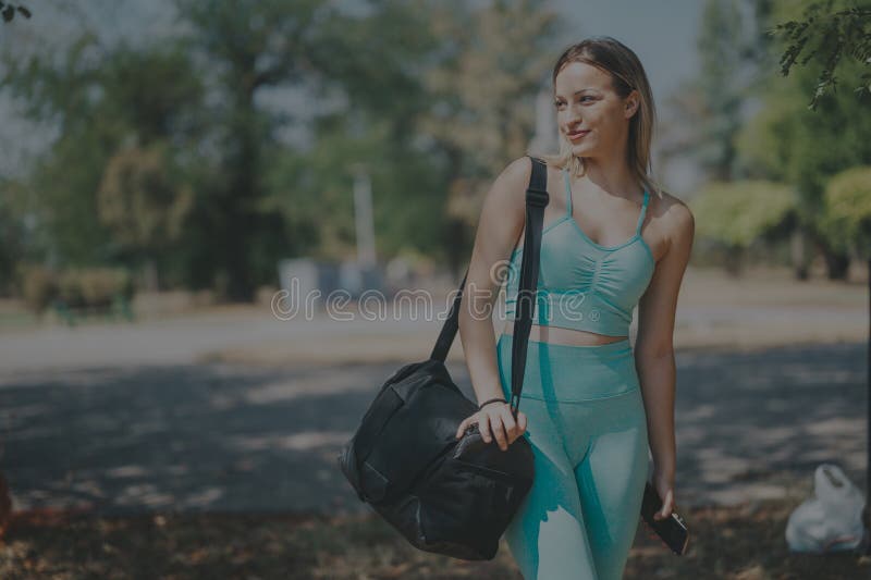Mujer con atuendo de yoga disfrutando de un día soleado en el parque. Una joven vestida de yoga en un parque con una bolsa disfrutando de un día soleado. el ambiente informal y relajado capta la esencia del ocio y el bienestar.