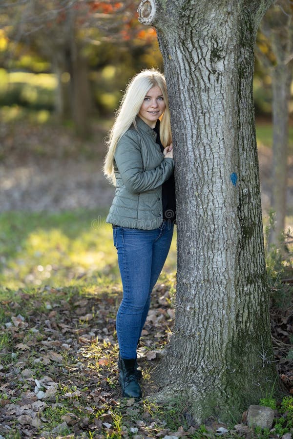 Mujer con cordones apoyándose en el árbol en los bosques. Una joven con cordones sonriendo inclinándose frente a un tronco de árbol en el bosque en un día soleado.