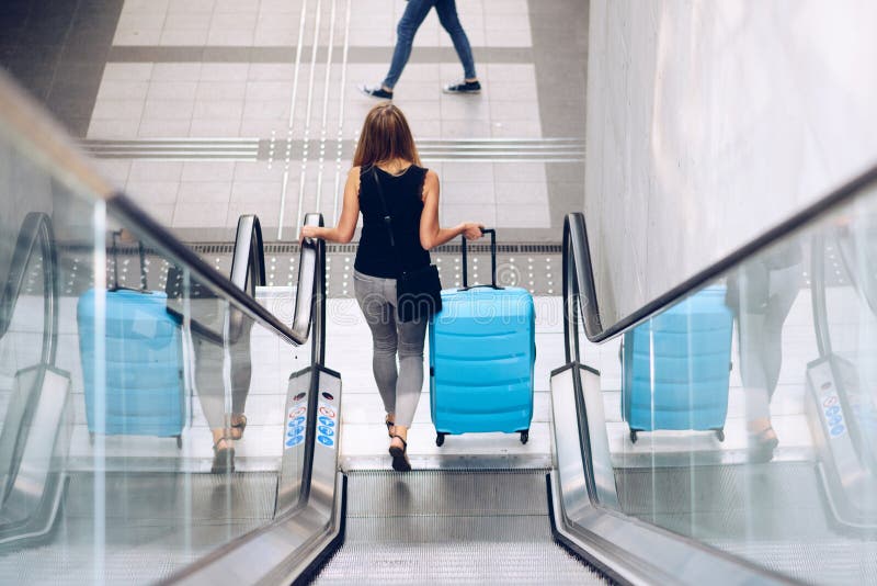 Mujer con la maleta azul del equipaje en la escalera móvil fotografía de archivo libre de regalías Mujer con la maleta azul del equipaje en la escalera móvil fotografía de archivo libre de regalías