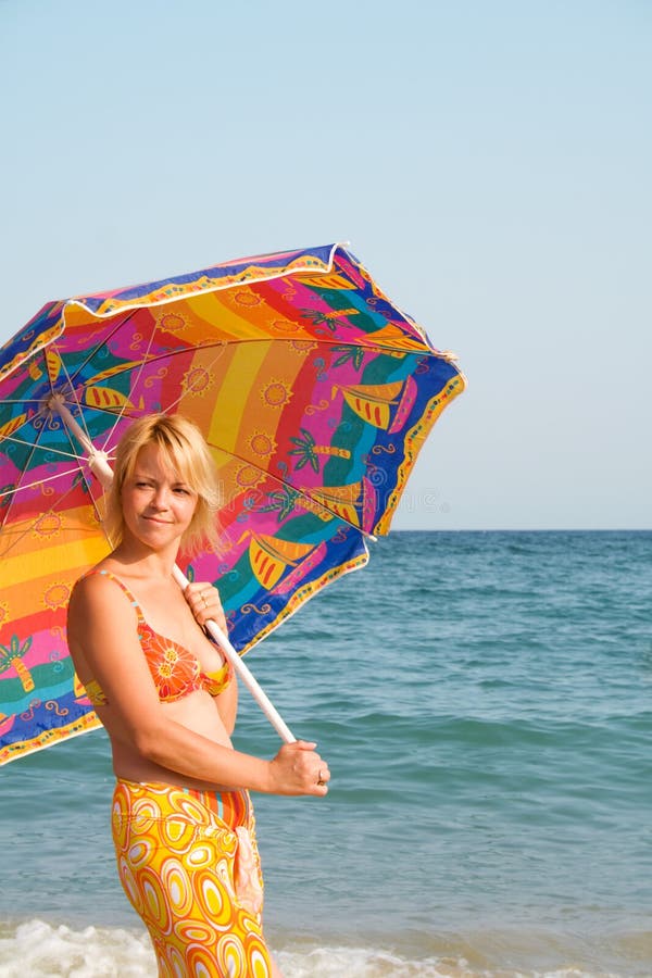 Woman with sunshade standing on the beach - striking summer colors - copyspace. Woman with sunshade standing on the beach - striking summer colors - copyspace