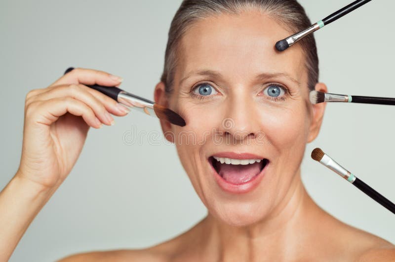 Portrait of funny mature woman with many brushes on face for makeup. Happy senior woman with a lot of makeup brushes near face and looking at camera. Cosmetic and beauty concept. Portrait of funny mature woman with many brushes on face for makeup. Happy senior woman with a lot of makeup brushes near face and looking at camera. Cosmetic and beauty concept.