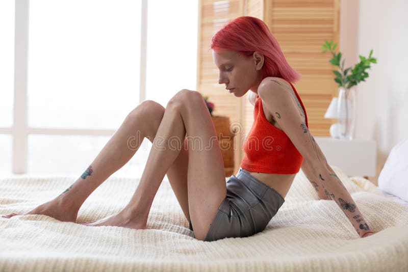 Mujer con los tatuajes que se sientan en cama mientras que siente mareado imagenes de archivo Mujer con los tatuajes que se sientan en cama mientras que siente mareado imagenes de archivo