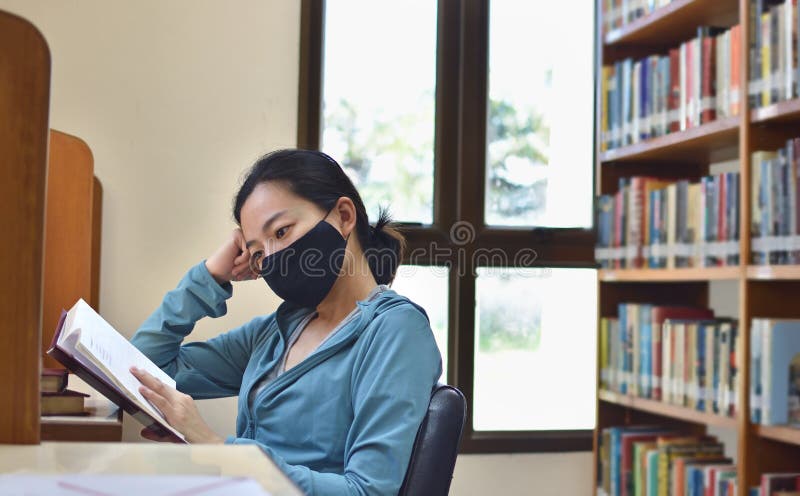 Mujer con máscara protectora leyendo un libro en la biblioteca imagen de archivo