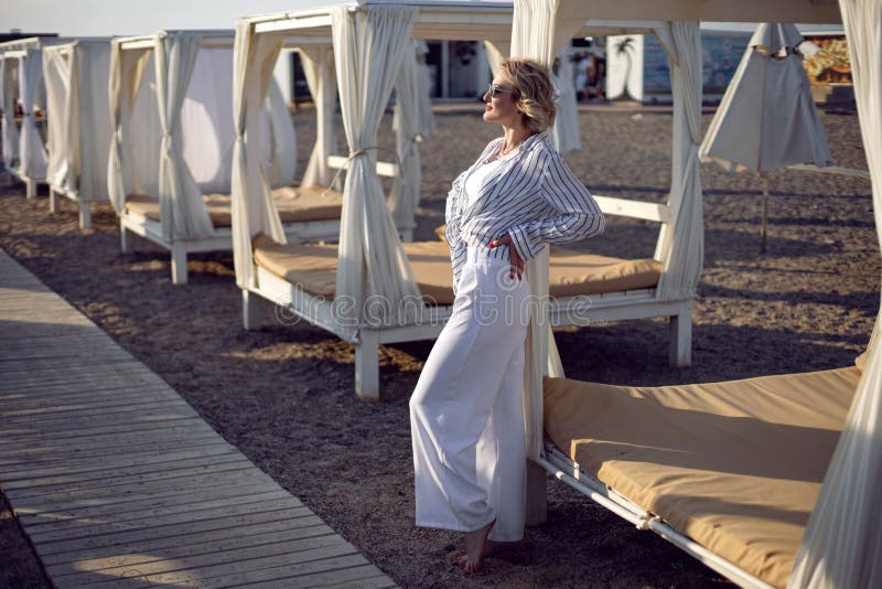 Mujer Con Ropa Blanca Y Gafas De Sol Está De Pie En La Playa Cerca Madera Foto de archivo - Imagen de lejos, 230717324