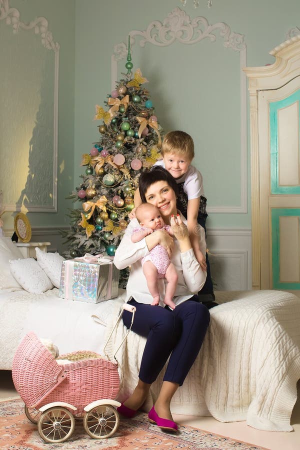 Mujer con un niño recién nacido en el cuarto de la Navidad un cochecito de niño imagen de archivo Mujer con un niño recién nacido en el cuarto de la Navidad un cochecito de niño imagen de archivo