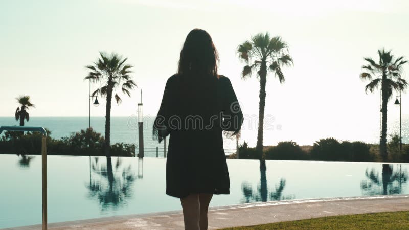 Mujer con visión trasera se saca de la bata de la playa mientras camina junto a la piscina almacen de video