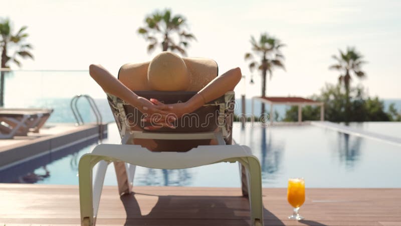 Mujer con vistas traseras relajante en una tumbona cerca de la piscina almacen de metraje de vídeo