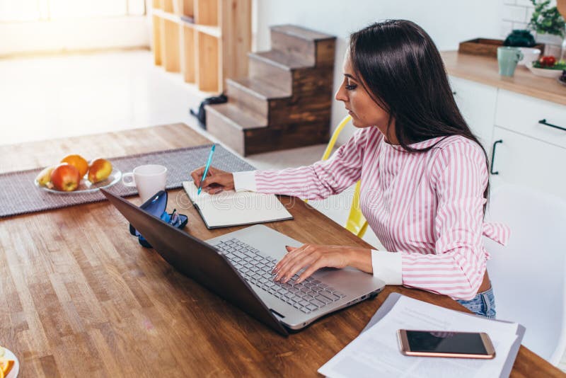 Mujer concentrada del freelancer que hace notas de Internet que trabaja a casa sentarse en la tabla fotografía de archivo