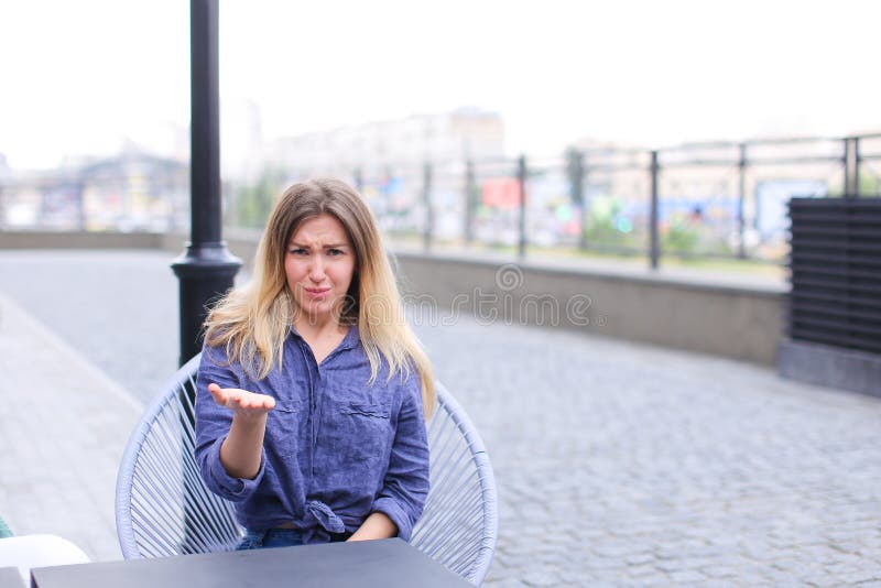 Mujer contrariedad joven que se sienta en el café de la calle y que hace caras