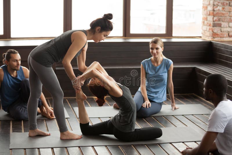 Mujer de ayuda del instructor de sexo femenino de la yoga que hace ejercicio en el tra del grupo