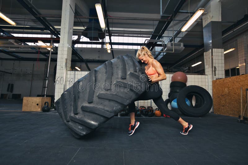 Mujer de Crossfit que mueve de un tirón un neumático enorme en el gimnasio
