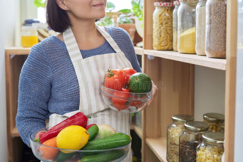 Organización de la mujer de la despensa en la cocina cerca del estante de  madera con latas y recipientes de comida.