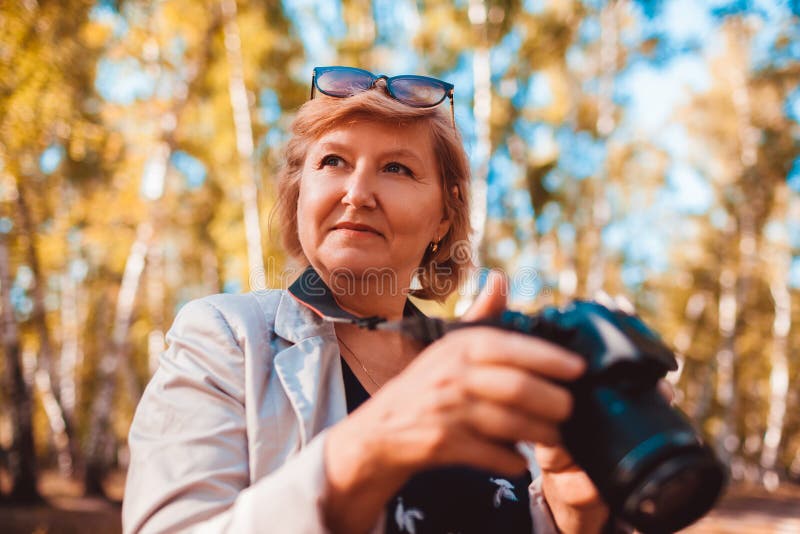 Mujer de mediana edad que comprueba imágenes en cámara en la mujer mayor del bosque del otoño que camina y que disfruta de la afi fotografía de archivo Mujer de mediana edad que comprueba imágenes en cámara en la mujer mayor del bosque del otoño que camina y que disfruta de la afi fotografía de archivo