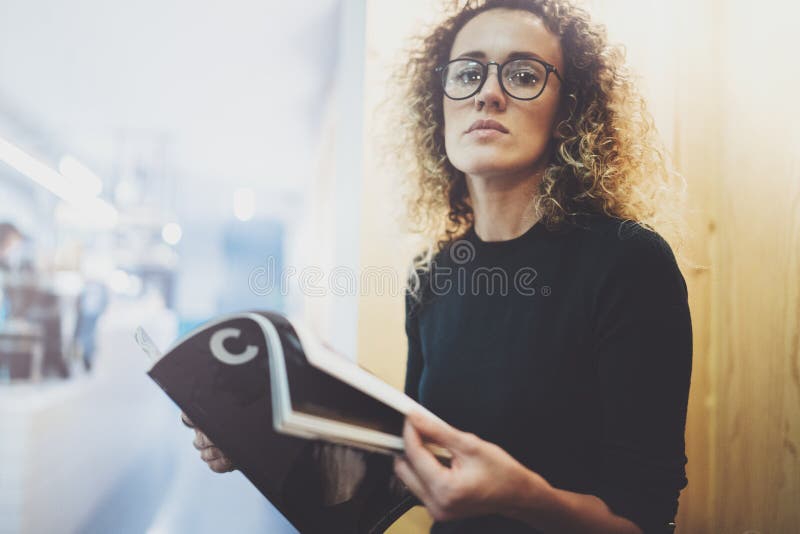 Mujer de moda encantadora con los vidrios de los ojos que lee sentarse de la revista interior en café urbano Retrato casual de ba fotos de archivo Mujer de moda encantadora con los vidrios de los ojos que lee sentarse de la revista interior en café urbano Retrato casual de ba fotos de archivo