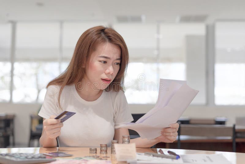 Mujer de negocios asiática chocada que sostiene la tarjeta de crédito que se sienta en el escritorio que mira el pago de las cuen fotos de archivo libres de regalías Mujer de negocios asiática chocada que sostiene la tarjeta de crédito que se sienta en el escritorio que mira el pago de las cuen fotos de archivo libres de regalías