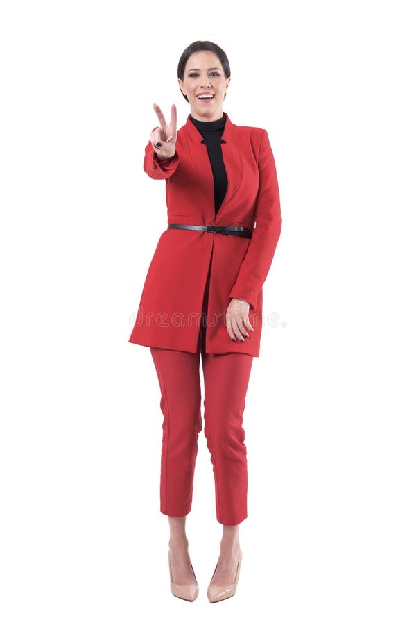 Mujer de negocios atractiva alegre en el traje rojo elegante que muestra la muestra de la victoria de dos fingeres o de la mano d fotos de archivo Mujer de negocios atractiva alegre en el traje rojo elegante que muestra la muestra de la victoria de dos fingeres o de la mano d fotos de archivo