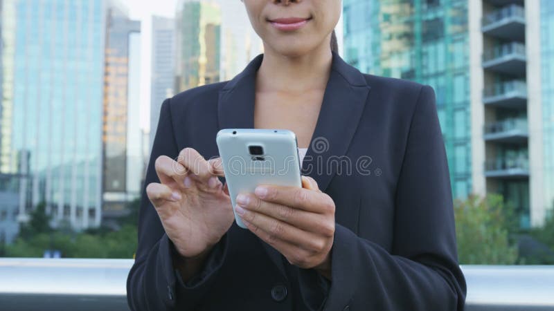 Mujer de negocios envía mensajes de texto desde una aplicación para smartphones en un distrito de negocios de la ciudad