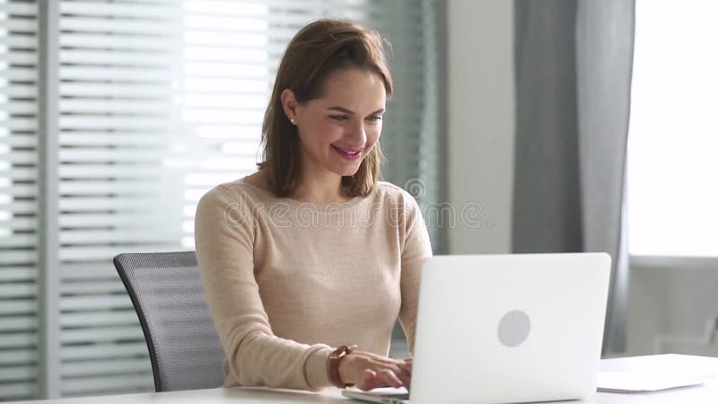 Mujer de negocios feliz usando el ordenador que comunica la sentada en línea en el escritorio metrajes