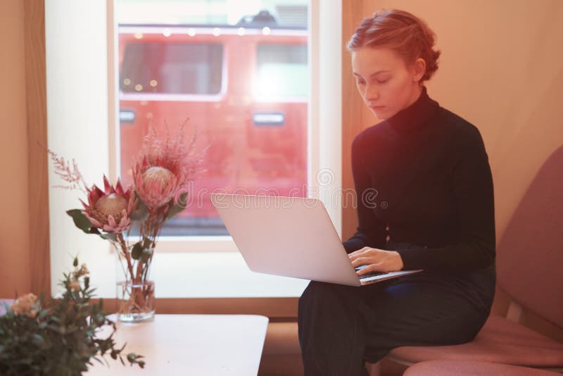 Mujer de negocios joven del inconformista que trabaja en el ordenador portátil, sentándose en café cerca de ventana, luz del día imágenes de archivo libres de regalías Mujer de negocios joven del inconformista que trabaja en el ordenador portátil, sentándose en café cerca de ventana, luz del día imágenes de archivo libres de regalías