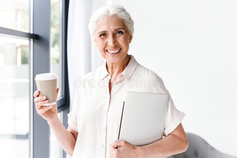 Mujer de negocios maduros feliz que sostiene el ordenador portátil imagen de archivo Mujer de negocios maduros feliz que sostiene el ordenador portátil imagen de archivo