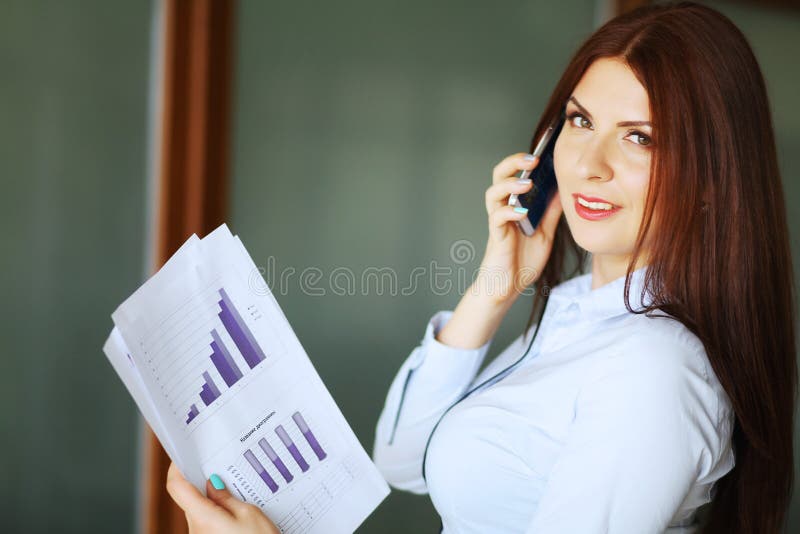Mujer de negocios que habla en el teléfono móvil, sonriendo y mirando la cámara Profundidad del campo baja foto de archivo Mujer de negocios que habla en el teléfono móvil, sonriendo y mirando la cámara Profundidad del campo baja foto de archivo