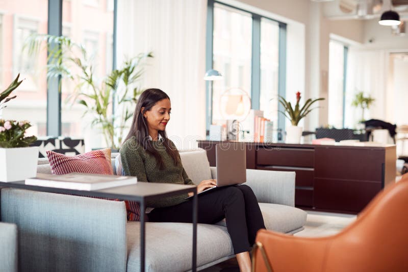 Mujer De Negocios Sentada En Sofá Trabajando En Portátil En Escritorio En Oficina De Ãrea De Trabajo Compartida fotos de archivo libres de regalías Mujer De Negocios Sentada En Sofá Trabajando En Portátil En Escritorio En Oficina De Ãrea De Trabajo Compartida fotos de archivo libres de regalías