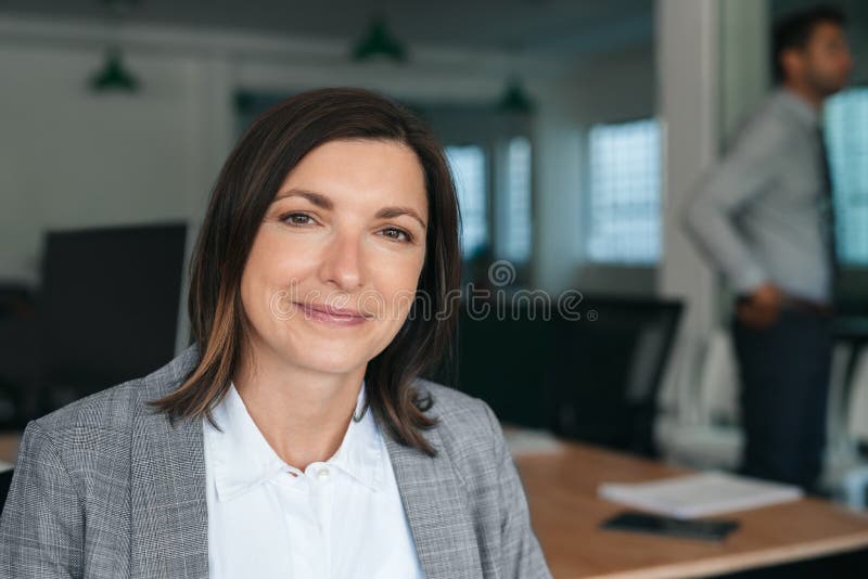 Mujer de negocios sonriente sentada en el trabajo con colegas de fondo fotos de archivo Mujer de negocios sonriente sentada en el trabajo con colegas de fondo fotos de archivo