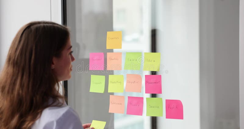 Mujer de negocios usa notas pegajosas en la pared de vidrio y escribe un plan de negocios estratégico metrajes