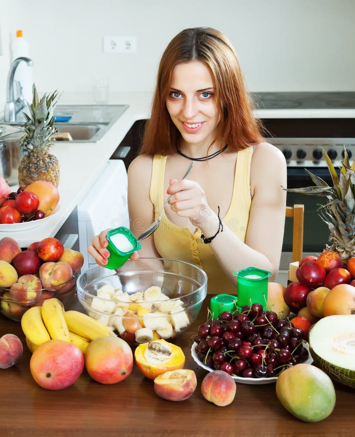 Mujer de pelo largo positiva que cocina la ensalada de fruta imágenes de archivo libres de regalías Mujer de pelo largo positiva que cocina la ensalada de fruta imágenes de archivo libres de regalías
