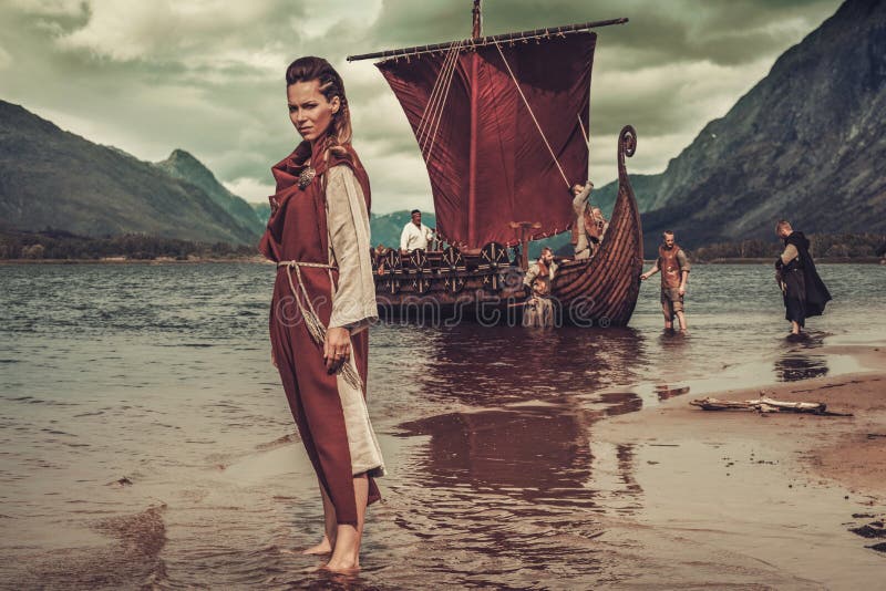 Mujer de Viking que se coloca cerca de Drakkar en la costa imagen de archivo Mujer de Viking que se coloca cerca de Drakkar en la costa imagen de archivo