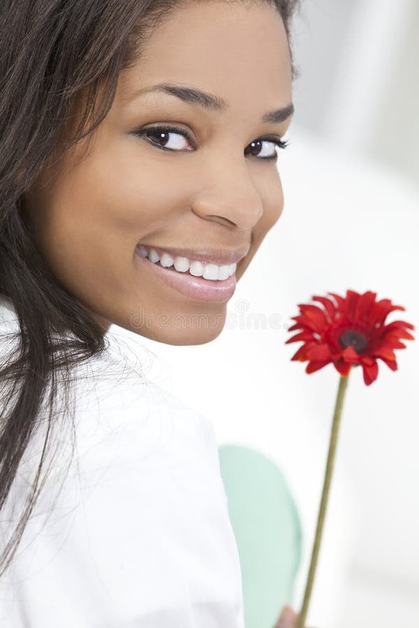 Mujer del afroamericano que sonríe con la flor roja imagen de archivo Mujer del afroamericano que sonríe con la flor roja imagen de archivo