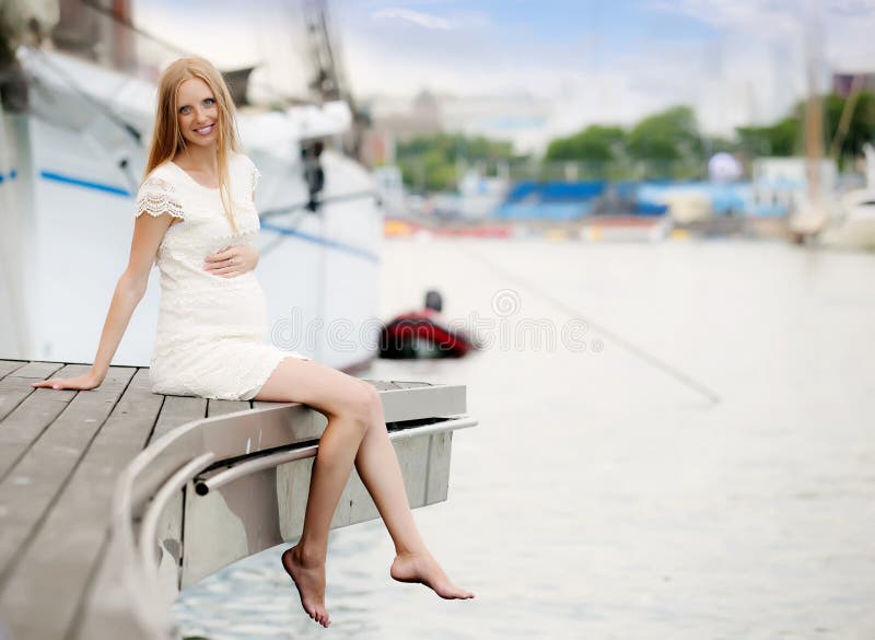 Mujer del embarazo que se sienta en el puerto fotografía de archivo Mujer del embarazo que se sienta en el puerto fotografía de archivo