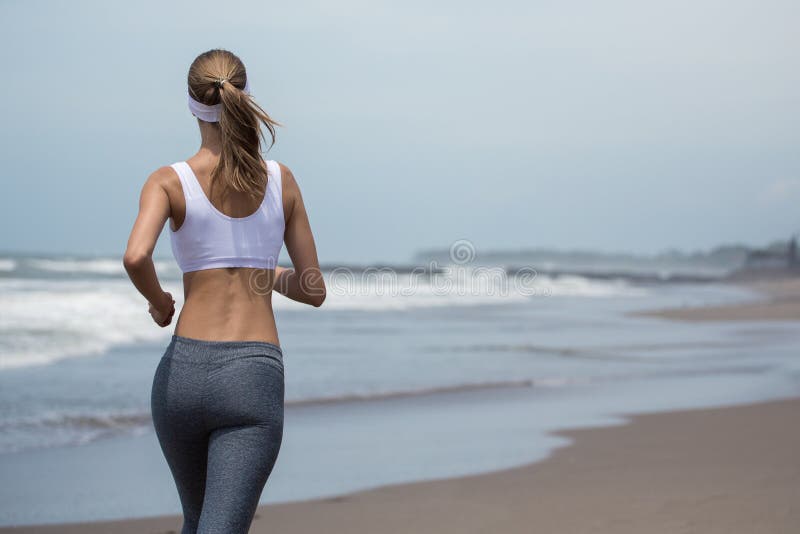 Mujer delgada joven que corre en la playa Visión posterior imagenes de archivo Mujer delgada joven que corre en la playa Visión posterior imagenes de archivo