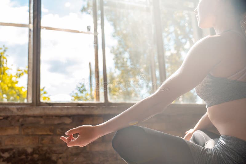 Mujer deportista tranquila sentada en loto posando haciendo yoga meditando en un gimnasio soleado