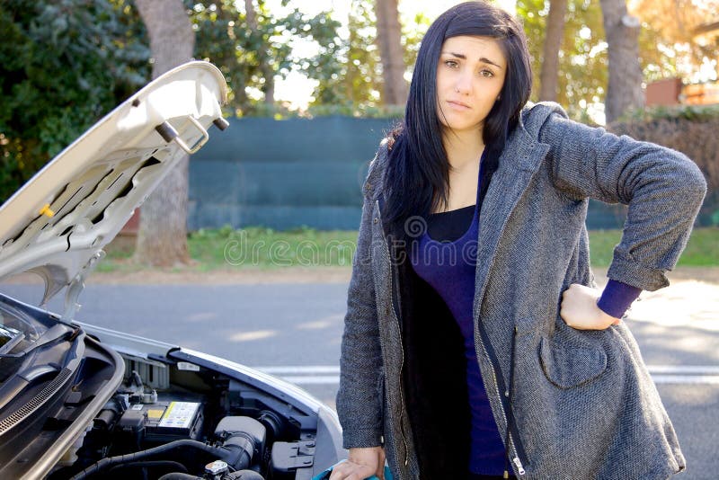 Mujer desesperada sobre el coche quebrado que mira la cámara fotos de archivo